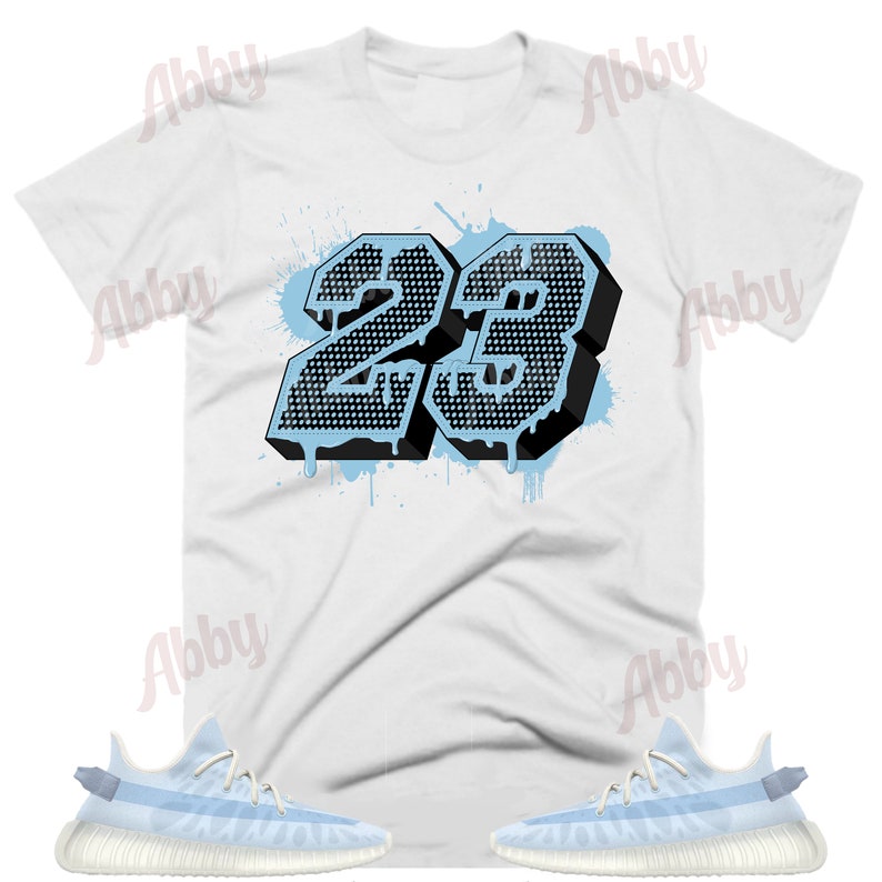 K&ouml;nnte beinhalten: Ein wei&szlig;es T-Shirt mit einer schwarzen und blauen Grafik der Nummer 23. Die Nummer tropft mit blauer Farbe. Das T-Shirt wird mit einem Paar hellblauer Sneakers mit wei&szlig;er Sohle kombiniert.