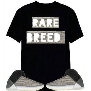 May include: A black t-shirt with the text "RARE BREED" printed on it. The shirt is paired with a pair of grey and black trainers.