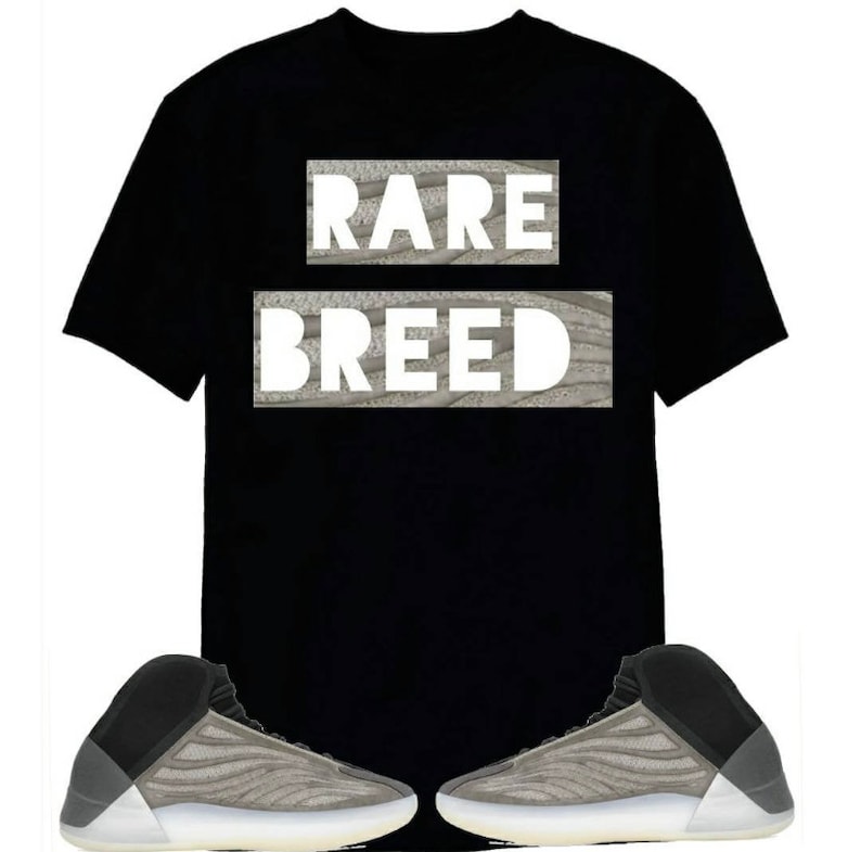 May include: A black t-shirt with the text "RARE BREED" printed on it. The shirt is paired with a pair of grey and black trainers.