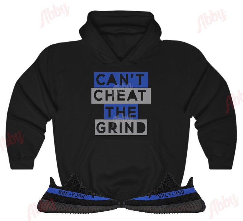 Może przedstawiać: Czarna bluza z kapturem z napisem "Can't Cheat The Grind" w niebieskich i szarych literach. Bluza jest połączona z czarnymi i niebieskimi butami sportowymi z napisem "SPLY-350" z boku.
