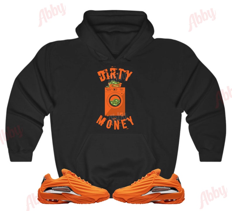 Peut inclure: Sweat-shirt &agrave; capuche noir avec un graphique d'une machine &agrave; laver remplie d'argent et le texte "Dirty Money". Le sweat-shirt est associ&eacute; &agrave; une paire de baskets orange.