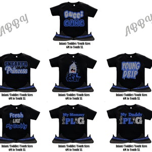 Puede incluir: Seis camisetas negras diferentes con varios dise&ntilde;os gr&aacute;ficos azules y plateados. Cada camiseta se combina con una zapatilla negra y azul. Las camisetas presentan dise&ntilde;os como "Gucci Gang", "Sneaker Princess", "Cry Baby", "Young Drip", "Fresh Like My Daddy" y "My Mommy is the PLG".
