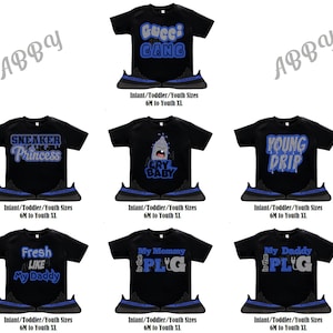 May include: Six different black t-shirts with various blue and silver graphic designs. Each shirt is paired with a black and blue sneaker. The shirts feature designs such as "Gucci Gang", "Sneaker Princess", "Cry Baby", "Young Drip", "Fresh Like My Daddy", and "My Mommy is the Plug".