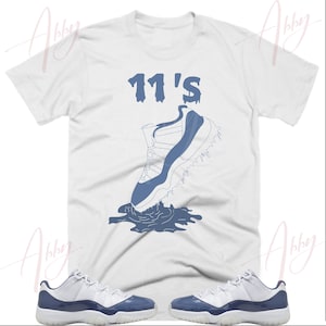 May include: A white t-shirt with a blue graphic of a basketball shoe with the text "11's" above it. A pair of white and blue basketball shoes are also shown.