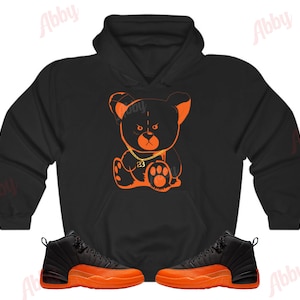 May include: Black hoodie with an orange cartoon bear wearing a gold chain with the number 23 on it. A pair of black and orange sneakers are also pictured.