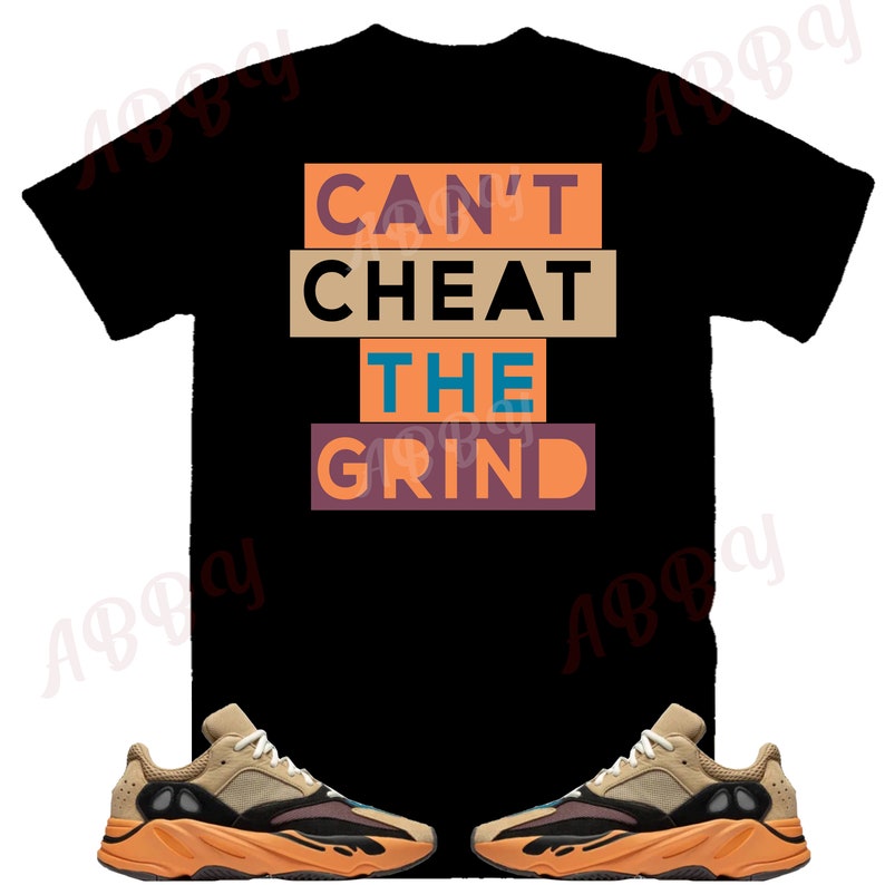May include: Black t-shirt with the text "Can't Cheat The Grind" in orange, brown, and blue. The shirt is paired with two tan and orange sneakers.