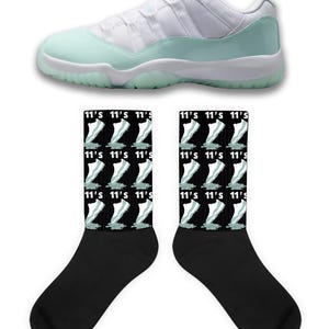 Puede incluir: Una zapatilla deportiva blanca y verde menta con calcetines a juego. Los calcetines son negros con un patrón repetido del diseño del zapato y el texto "11's". El zapato tiene una parte superior blanca y una suela verde menta.