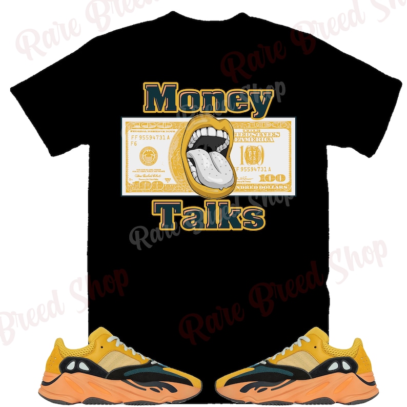 May include: A black t-shirt with a yellow and green graphic of a dollar bill with a mouth and tongue sticking out. The text "Money Talks" is printed below the graphic. Two yellow, black, and orange sneakers are shown below the t-shirt.