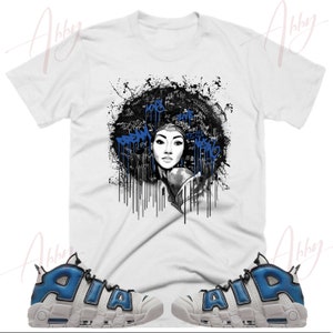 May include: White t-shirt with a black and white graphic of a woman with an afro and blue paint splatters. The graphic has text that says "Dream Big" and "Live Your Truth". The t-shirt is paired with white and blue sneakers.