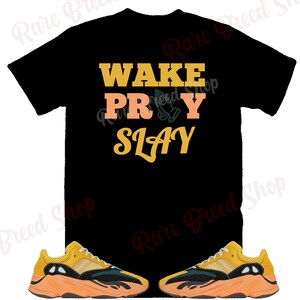 May include: Black t-shirt with the text "WAKE PRAY SLAY" in yellow and orange lettering. A pair of yellow and orange sneakers with black accents.