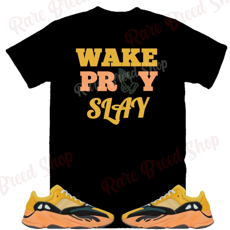 May include: Black t-shirt with the text "WAKE PRAY SLAY" in yellow and orange lettering. A pair of yellow and orange sneakers with black accents.