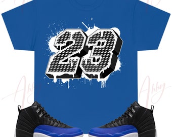 May include: A royal blue t-shirt with a white graphic of the number 23 in a dripping paint style. The shirt is paired with black and royal blue sneakers.