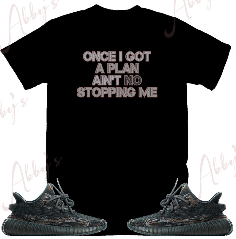 Puede incluir: Camiseta negra con el texto "ONCE I GOT A PLAN AIN'T NO STOPPING ME" en letras blancas y grises. Tambi&eacute;n se muestra un par de zapatillas de deporte de camuflaje negro y verde.
