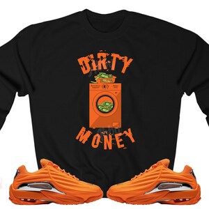 Peut inclure: Sweat-shirt noir avec le texte "DIRTY MONEY" et un graphique d'une machine &agrave; laver remplie d'argent. Le sweat-shirt est associ&eacute; &agrave; des baskets orange et argent.