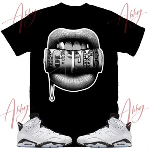 May include: Black t-shirt with a graphic of a mouth biting a roll of money. The mouth is dripping with a liquid.  Two white and black sneakers with a black and white speckled sole.