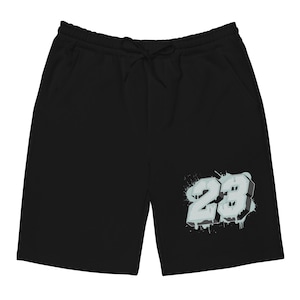 Puede incluir: Pantalones cortos negros con cintura con cordón y bolsillos. Los pantalones cortos presentan un gráfico del número "23" en un diseño de estilo grafiti con un esquema de color blanco y azul claro.