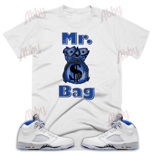 May include: White t-shirt with a blue money bag graphic and the text "Mr. Bag".  A pair of white and blue sneakers with a blue swoosh.