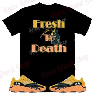 Pu&ograve; includere: Maglietta nera con il testo "Fresh to Death" in arancione e una grafica della Morte. Un paio di scarpe da ginnastica gialle e nere con suole arancioni.