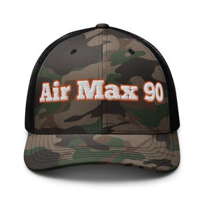 May include: A black and camouflage trucker hat with the text "Air Max 90" embroidered in white with orange outlining.