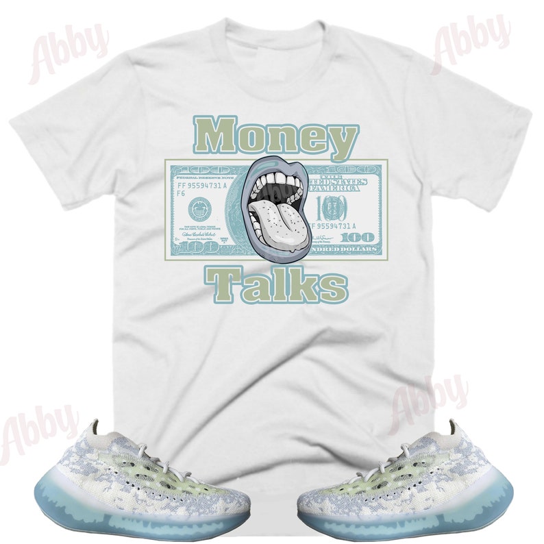 Pode incluir: Camiseta branca com a frase "Money Talks" em verde e um desenho de uma boca e l&iacute;ngua em uma nota de 100 d&oacute;lares. A imagem tamb&eacute;m mostra um par de t&ecirc;nis brancos e azul claro com sola transl&uacute;cida.