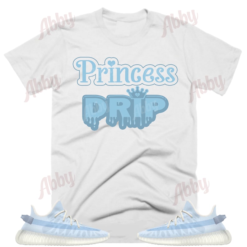 K&ouml;nnte beinhalten: Wei&szlig;es T-Shirt mit blauem Text, der "Princess Drip" mit einer Krone &uuml;ber dem Wort "Drip" sagt. Das Shirt wird mit einem Paar hellblauer und wei&szlig;er Turnschuhe kombiniert.