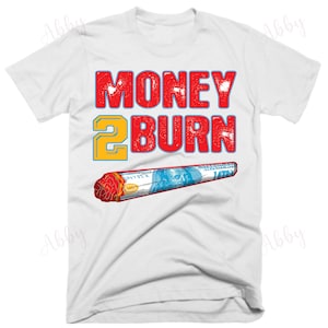 May include: White t-shirt with red text that says "MONEY 2 BURN" and a graphic of a rolled-up dollar bill with a red tip.