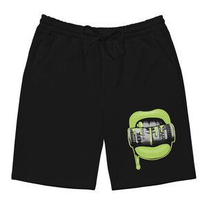 Puede incluir: Pantalones de chándal negros con un gráfico de boca verde. La boca sostiene una pila de billetes de dólar.