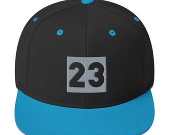 May include: A black and blue baseball cap with a white square patch that says "23" in black.