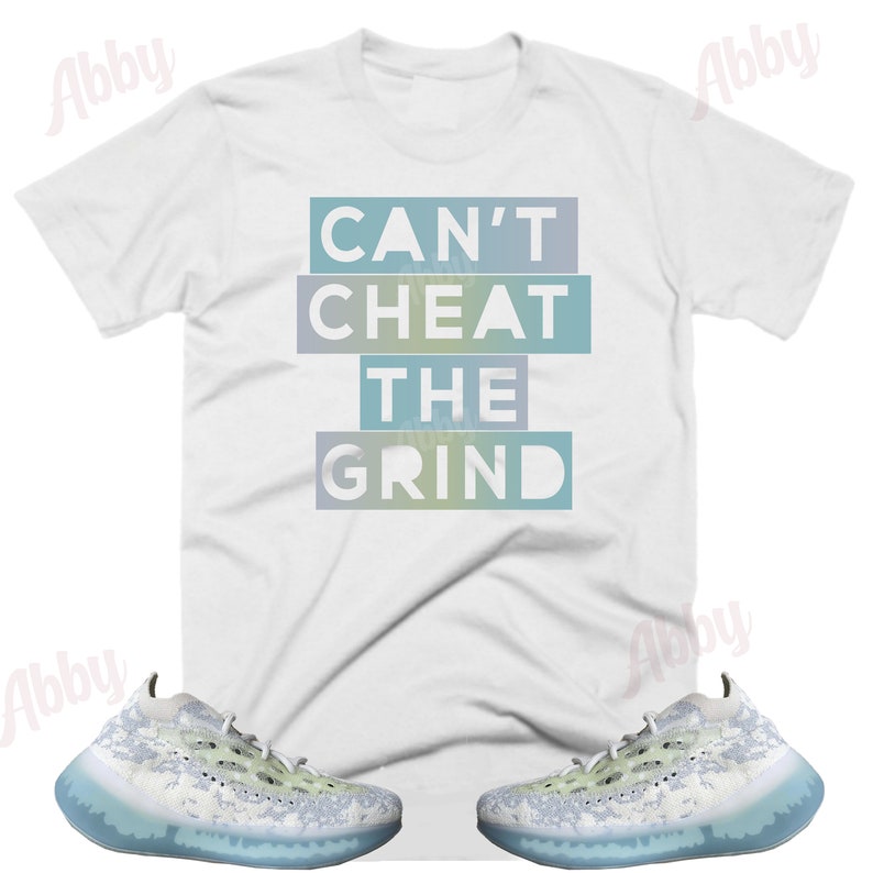 May include: White t-shirt with the text "CAN'T CHEAT THE GRIND" in a blue and green gradient. The shirt is paired with a pair of white and light blue sneakers with a speckled pattern.