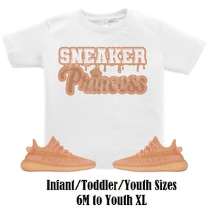 May include: White t-shirt with the text "Sneaker Princess" in brown dripping letters.  A pair of peach-colored sneakers with white laces.