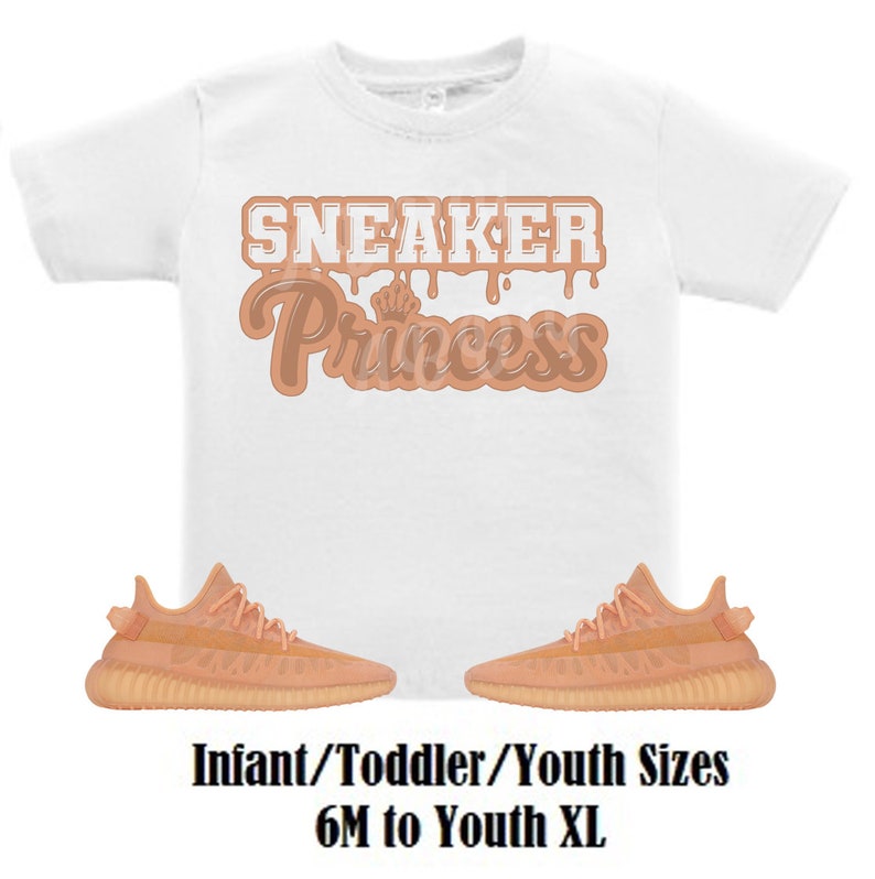 May include: White t-shirt with the text "Sneaker Princess" in brown dripping letters.  A pair of peach-colored sneakers with white laces.