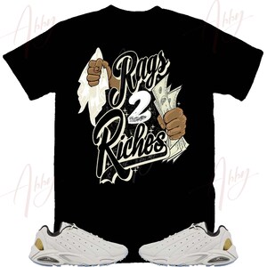 May include: A black t-shirt with the text "Rags 2 Riches" in white and gold lettering. The shirt features a graphic of a hand holding money and another hand wiping away dirt. A pair of white sneakers with gold accents are also pictured.