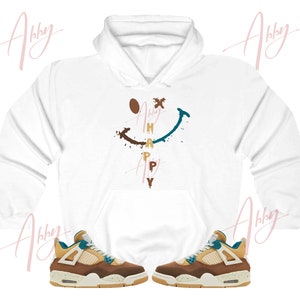 May include: White hoodie with a smiley face graphic and the word "HAPPY" written vertically inside the face. The hoodie is paired with a pair of brown and teal sneakers.