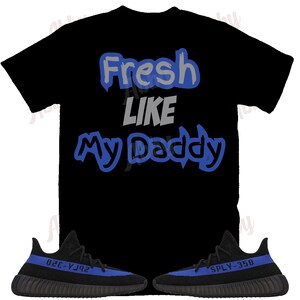 Puede incluir: Camiseta negra con texto azul y gris que dice "Fresh Like My Daddy". Un par de zapatillas negras y azules con el texto "SPLY-350" y "350-Y3J2" en las suelas.