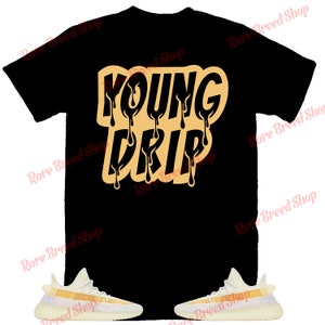 以下が含まれることがあります： 「YOUNG DRIP」という文字がオレンジとイエローの滴るフォントで書かれた黒いTシャツ。白いオレンジ色のスニーカーと合わせています。