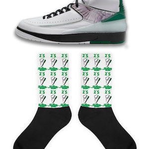 May include: A pair of black socks with a white design featuring a repeated pattern of green and white sneakers with the text "2'S" on them. A white and green sneaker with a white wing design is also pictured.