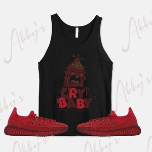 Puede incluir: Una camiseta sin mangas negra con un gr&aacute;fico de biber&oacute;n rojo de dibujos animados y el texto "CRY BABY". Dos pares de zapatillas rojas con detalles negros.
