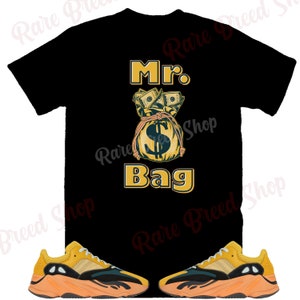 May include: Black t-shirt with the text "Mr. Bag" and a cartoon image of a money bag with dollar bills. Two yellow and orange trainers with black accents.