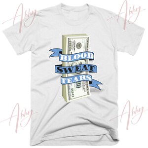May include: White t-shirt with a stack of hundred dollar bills and the text "Blood Sweat Tears" on a blue ribbon.