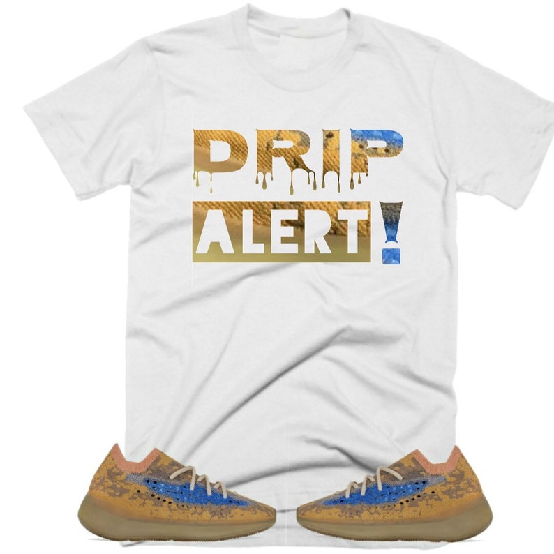 May include: White t-shirt with the text "DRIP ALERT!" in a dripping font with a desert-like pattern. The shirt is paired with a pair of tan and blue sneakers.