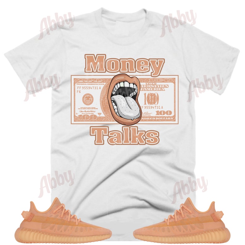 Może przedstawiać: Biały t-shirt z grafiką przedstawiającą usta z wystającym językiem, nałożoną na banknot 100 dolarowy. Pod grafiką znajduje się tekst "Money Talks". Pod t-shirtem widoczne są dwie pary beżowych but&oacute;w sportowych.
