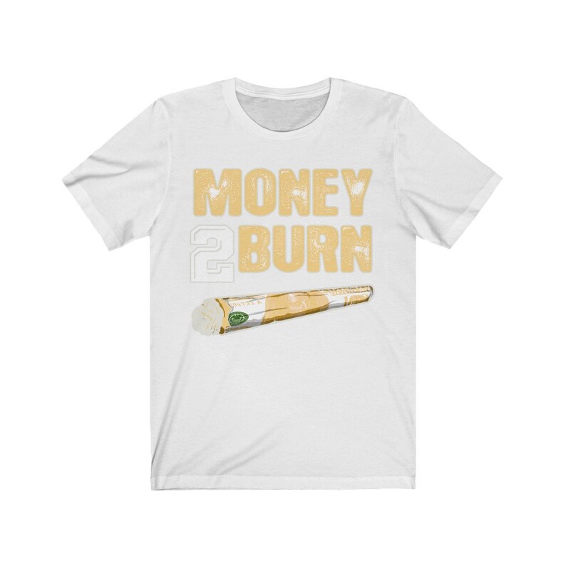 Puede incluir: Camiseta blanca con el texto "MONEY 2 BURN" en letras doradas y una imagen de dibujos animados de un porro enrollado.