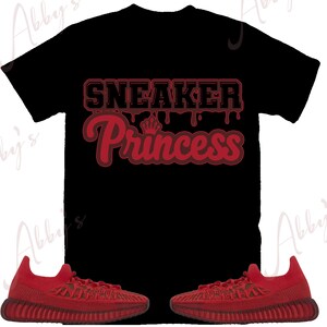 Peut inclure: T-shirt noir avec le texte "SNEAKER Princess" en rouge et un petit motif de couronne. Deux baskets rouges sont en bas de l'image. Les baskets ont un design textur&eacute;.