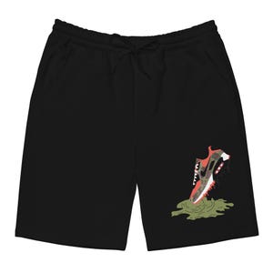 May include: Black athletic shorts featuring a graphic print of a red, green and black trainer stepping in a green puddle.