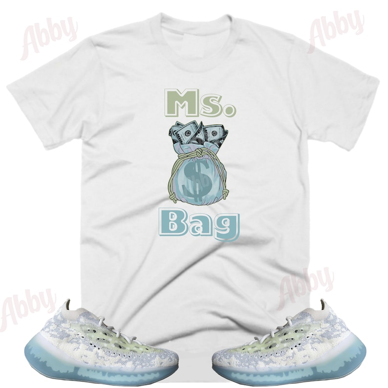 Puede incluir: Camiseta blanca con un gr&aacute;fico de una bolsa de dinero con el texto "Ms. Bag". Un par de zapatillas blancas y azul claro con un patr&oacute;n de camuflaje.