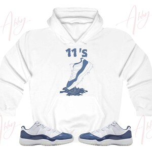 May include: White hoodie with a blue graphic of a basketball shoe with the text "11's" above it. A pair of blue and white basketball shoes are also pictured.