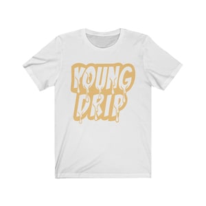 以下が含まれることがあります： 「YOUNG DRIP」という文字が滴るように描かれた、金色のグラフィックがプリントされた白いTシャツです。