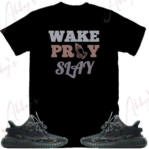 May include: Black t-shirt with the words "WAKE PRAY SLAY" in gray and brown lettering. The word "PRAY" features a graphic of praying hands. Two pairs of black and brown sneakers are at the bottom of the image.