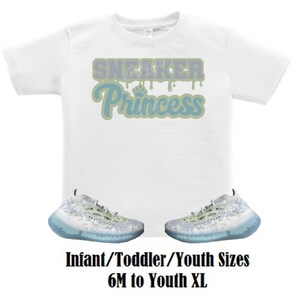May include: White t-shirt with the text "Sneaker Princess" in blue and green dripping letters. Two pairs of white and light blue sneakers with a speckled pattern.
