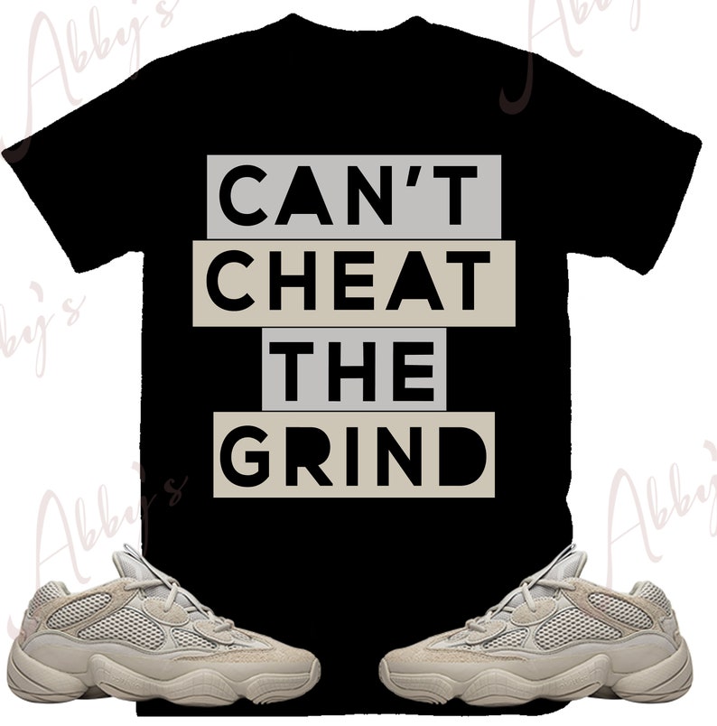 Puede incluir: Una camiseta negra con el texto "Can't Cheat The Grind" en letras blancas y beige. Dos pares de zapatillas beige est&aacute;n a cada lado de la camiseta.